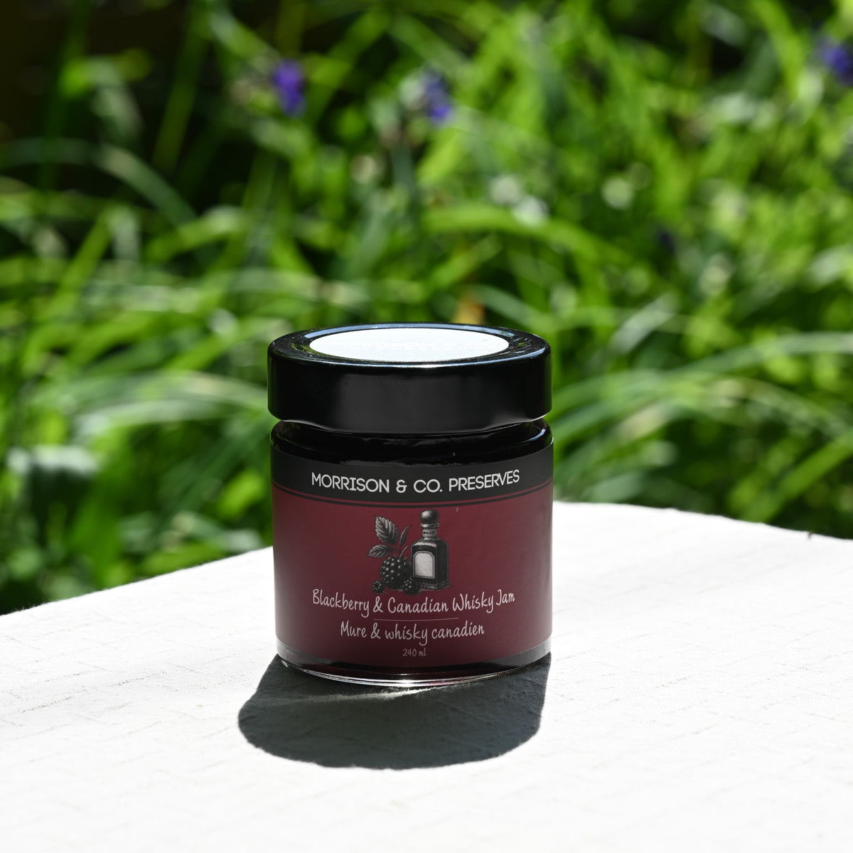 Jar of Morrison & Co. Preserves Blackberry and Canadian Whisky Jam on a white surface with a green, blurred background