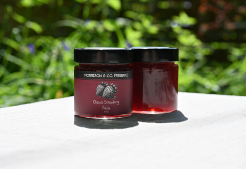 Two jars of classic Morrison & Co Preserves strawberry jam with a blurred green background