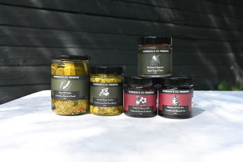 Five jars of Morrison & Co Preserves arranged on a white tablecloth against a dark wooden background.