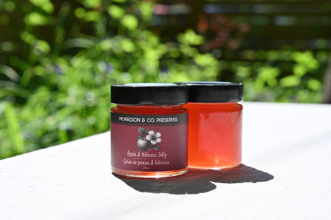 Two jars of apple and hibiscus tea jelly with a blurred green outdoor background
