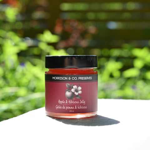 Jar of Morrison & Co. Preserves Apple & Hibiscus Jelly with a blurred green garden background