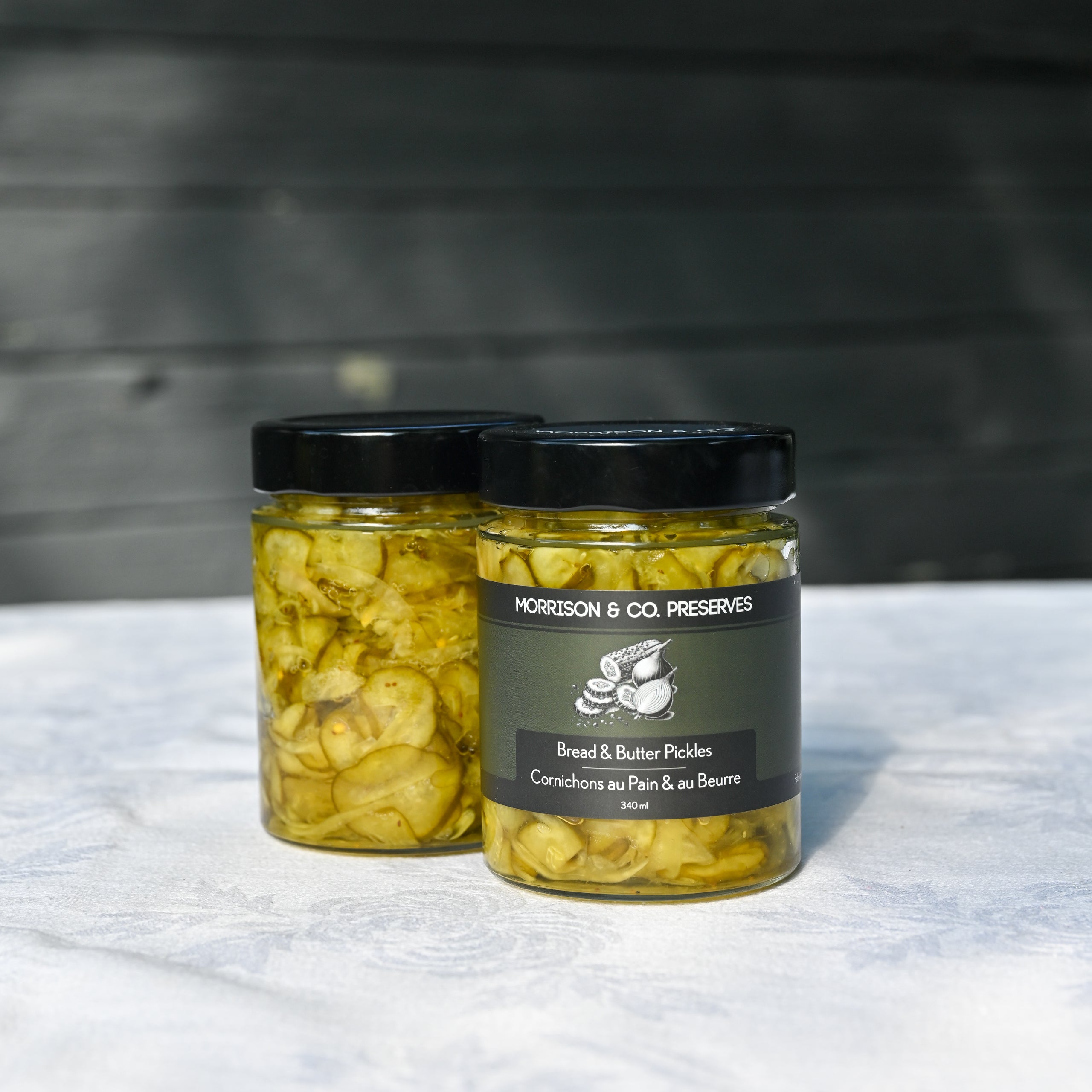 Two jars of Morrison & Co Preserves Bread & Butter pickles on a white tablecloth