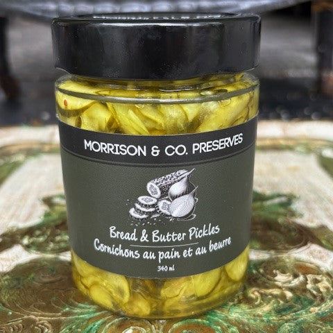 Jar of bread and butter pickles with a black lid and label on a decorative surface.
