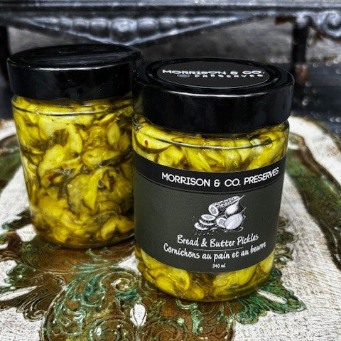 Two jars of Morrison & Co. Preserves bread and butter pickles on a decorative surface