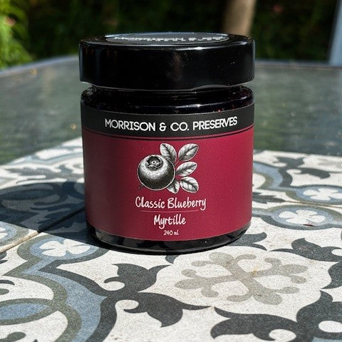 Jar of Morrison & Co. Preserves Classic Blueberry on a patterned table outdoors.
