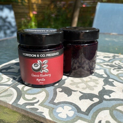 Two jars of Morrison & Co. Blueberry Preserves on a patterned table outdoors.