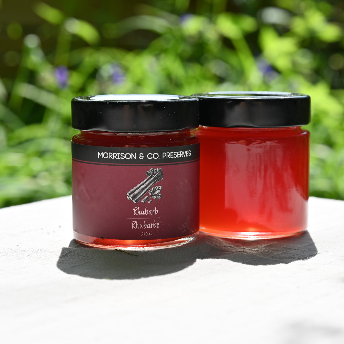 Two jars of rhubarb preserve with a blurred green outdoor background
