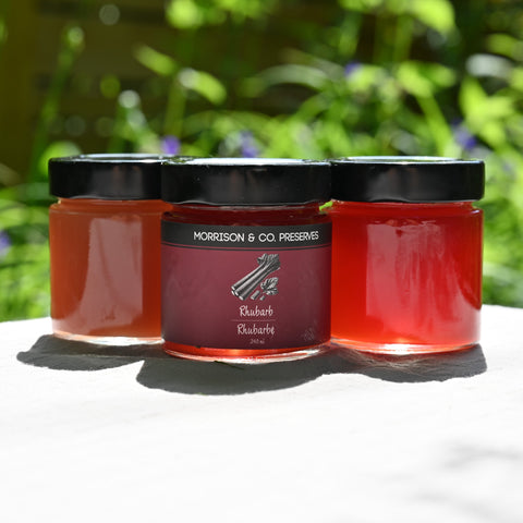 Three jars of rhubarb conserve with a blurred green outdoor background