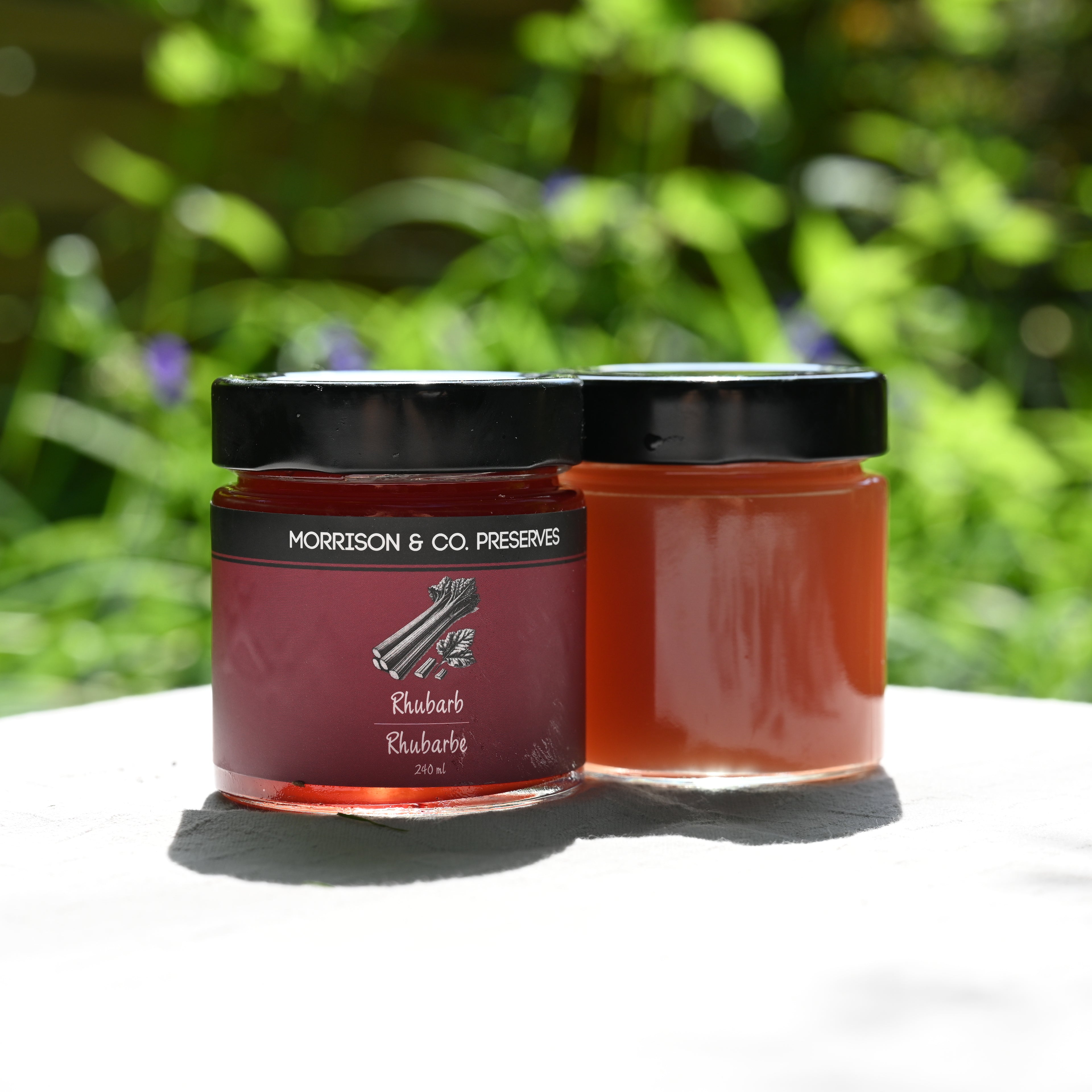 Two jars of rhubarb conserve with a blurred green background
