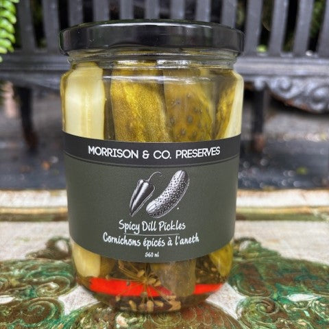 Jar of Morrison & Co. Preserves Spicy Dill Pickles on a decorative surface with a blurred background.