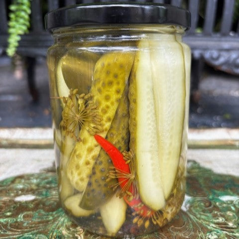 Jar of spicy dill pickles with a black lid on a decorative surface.